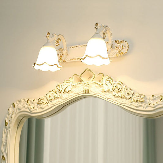 Weiße Vintage-Wandleuchte mit zwei Lampenschirmen über verziertem Spiegel, klassisches Design.