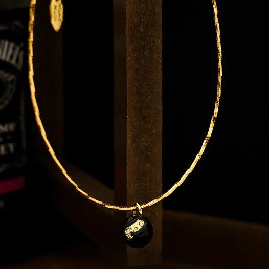 Goldene Halskette mit schwarzem Anhänger, elegantes Schmuckdesign, luxuriöses Accessoire.