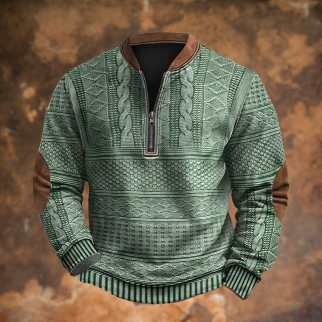 Grön tröja med kabelstickat mönster, halvdragkedja, brun krage och bruna armbågslappar, sedd framifrån mot rostbrun bakgrund. 6