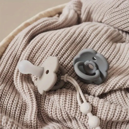 Beige Babydecke mit grauem und weißem Silikon-Schnuller auf Strickstoff.