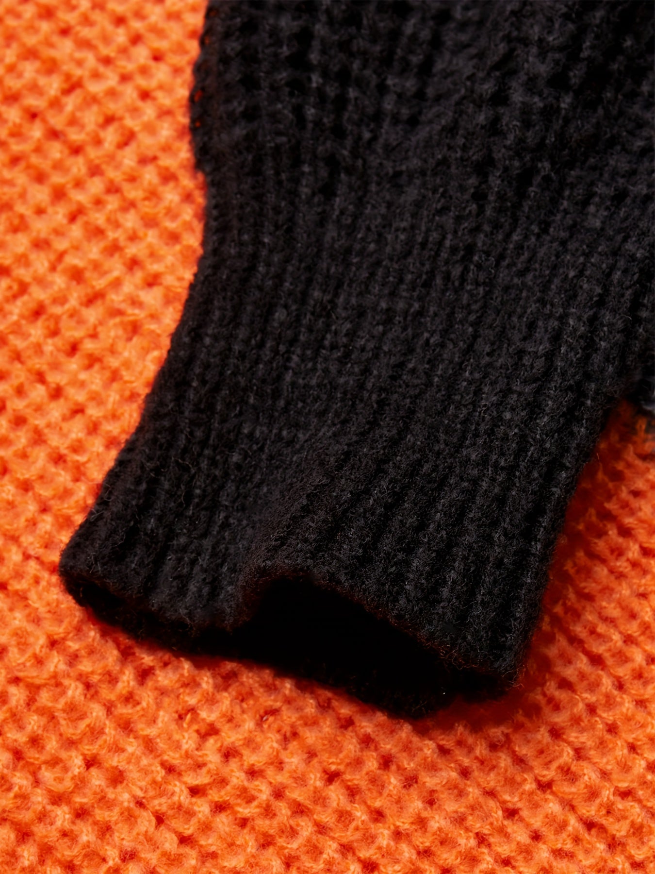 Schwarzer Strickpulloverärmel auf orangefarbenem Strickhintergrund, warme Wintermode.