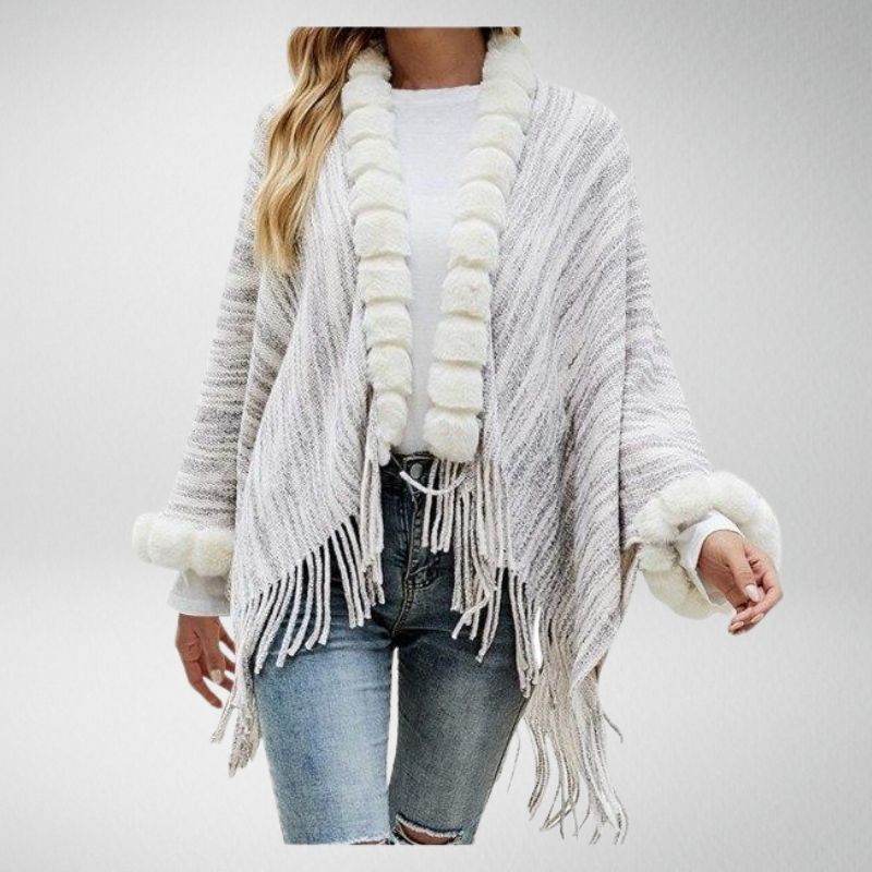 Frau in grauem Strickponcho mit Fransen und weißem Kunstfell, lässige Mode.