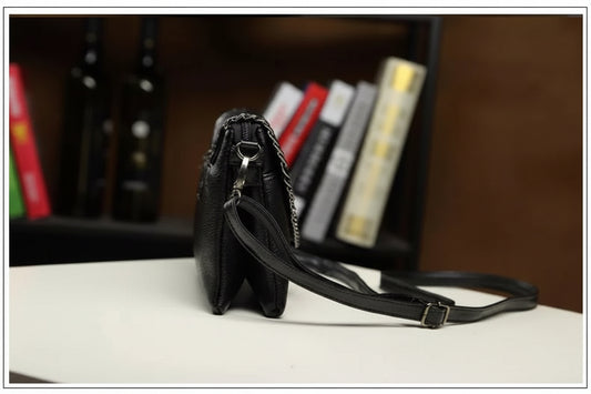Schwarze Ledertasche mit verstellbarem Riemen, seitliche Ansicht, auf Tisch vor Bücherregal.