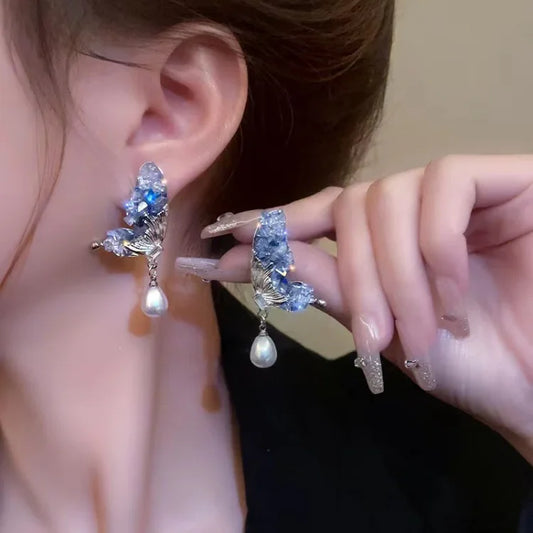 Frau mit blauen Kristall-Ohrringen und Perlenanhänger, eleganter Schmuck, Nahaufnahme.