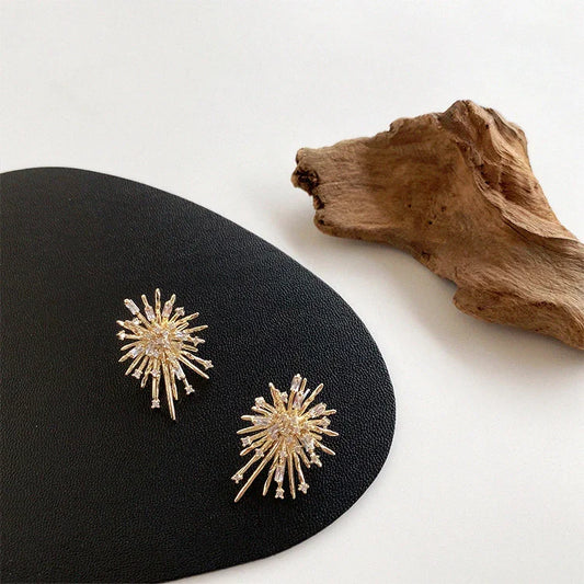 Goldene Sonnenstrahl-Ohrringe auf schwarzem Leder, eleganter Schmuck, modernes Design.