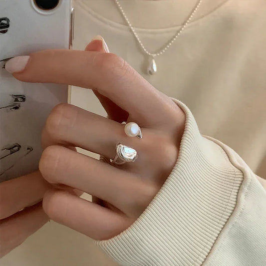 Damenhand mit Perlenring und Silberring, Smartphone, cremefarbener Pullover, Perlenkette.