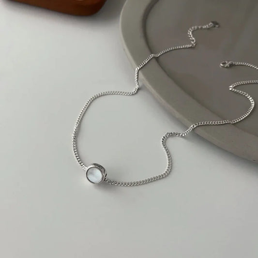 Silberne Halskette mit rundem Anhänger auf grauem Teller, minimalistischer Schmuck, elegant.
