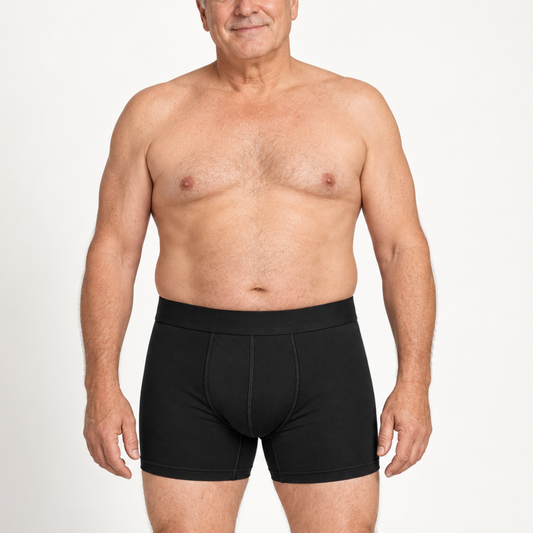 Äldre man med bar överkropp står rakt framifrån i svarta boxerkalsonger med längre ben och bred midjelinning. 2