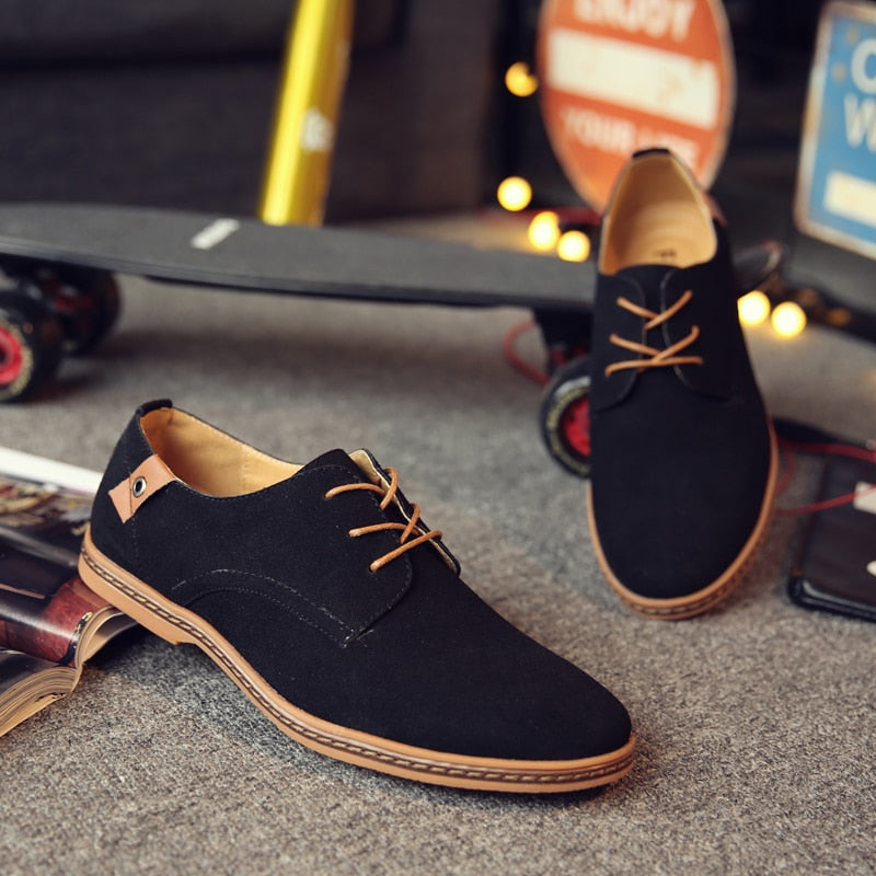 Schwarze Herren-Sneaker aus Wildleder mit braunen Schnürsenkeln auf grauem Teppich.