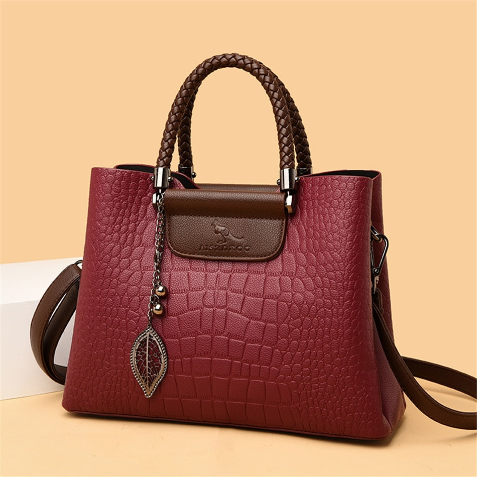 Damenhandtasche aus rotem Leder mit Krokodilprägung, braunen Griffen und Blattanhänger.