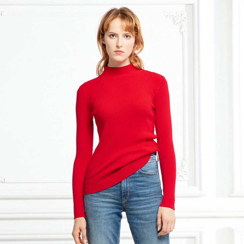 Frau in rotem Rollkragenpullover und blauer Jeans vor weißer Wand.