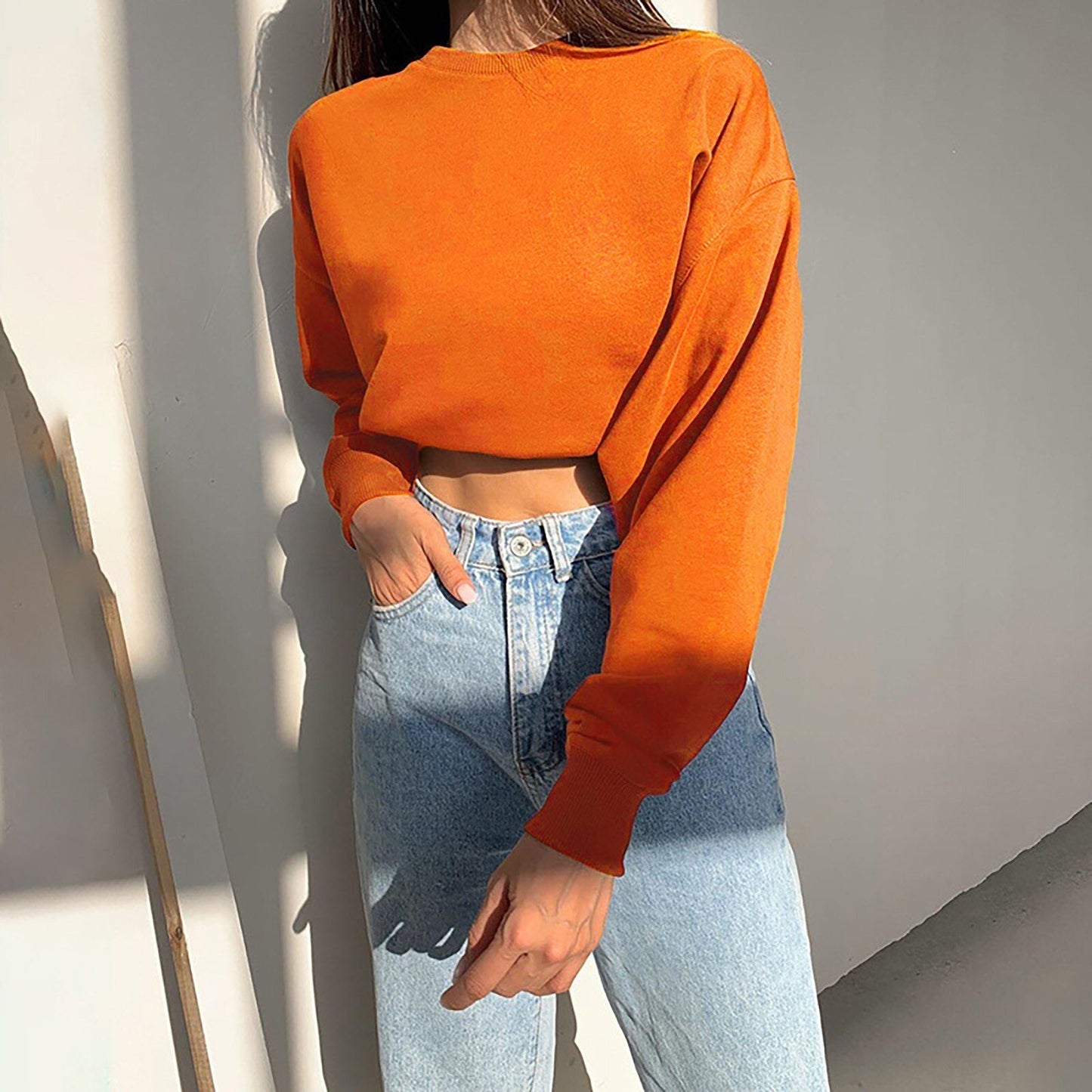 Frau in orangefarbenem Crop-Top und blauer Jeans, lässige Mode, Herbstoutfit.