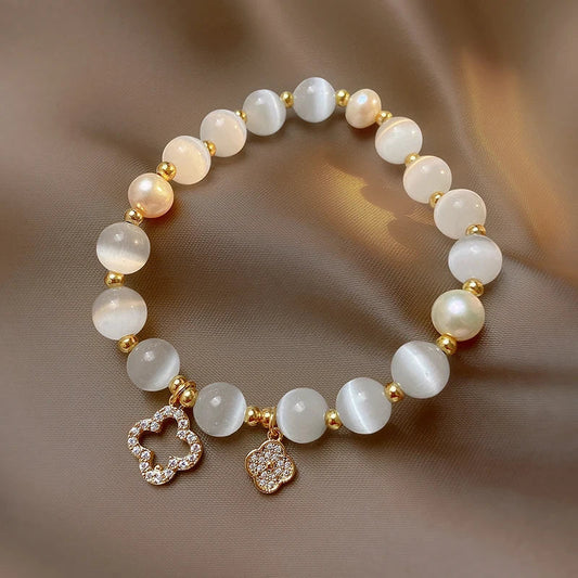 Armband aus weißen Perlen mit goldenen Akzenten und Blumenanhängern, eleganter Schmuck.