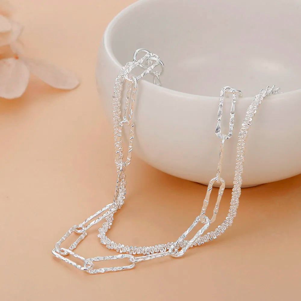 Silberne Halskette mit Gliederketten-Design, eleganter Schmuck auf beigem Hintergrund.