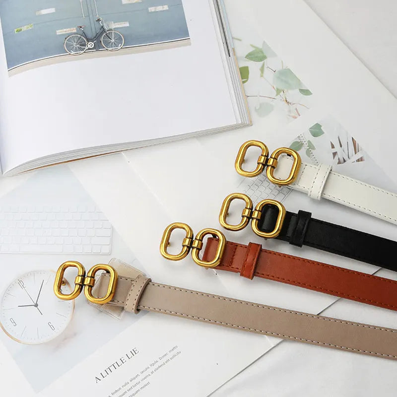 Vier Retro-Gürtel mit goldener Schnalle in Weiß, Schwarz, Braun und Beige auf einem Tisch.