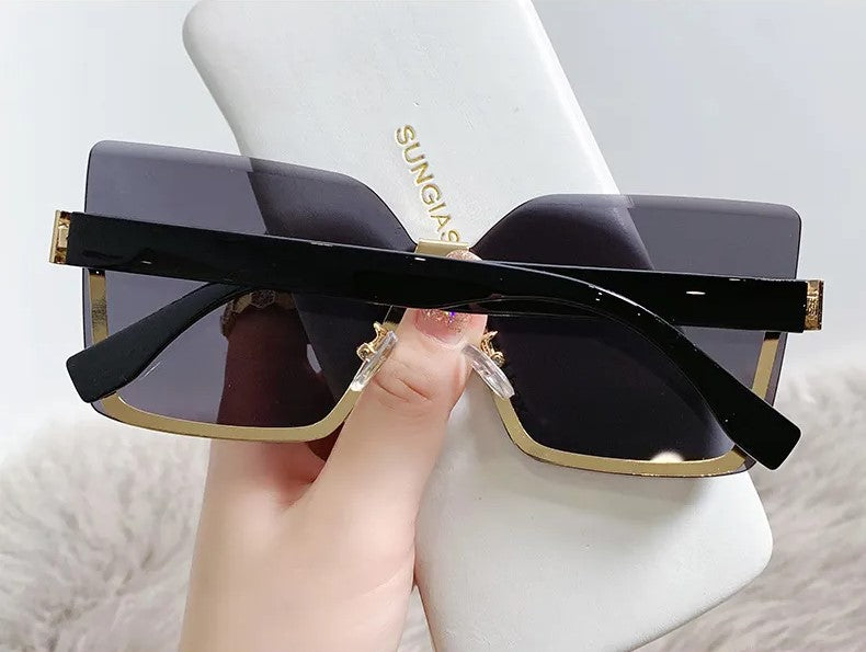 Schwarze übergroße Sonnenbrille mit goldenen Akzenten, rechteckig, in Hand gehalten.