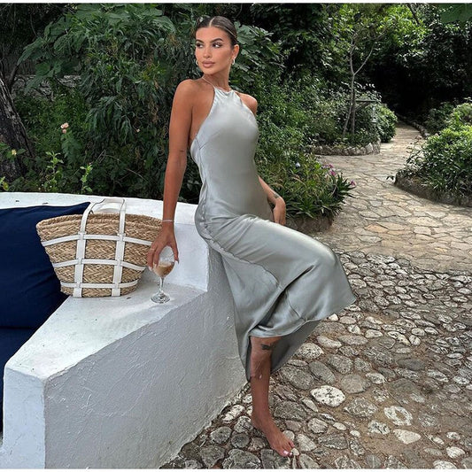 Frau in silbernem Satin-Kleid, sitzt draußen, hält Weinglas, Sommermode, elegantes Outfit.