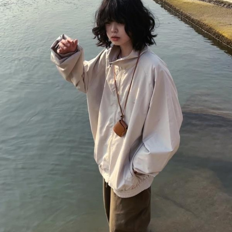 Frau in beiger Oversize-Jacke am Wasser, modischer Herbstlook, lässiger Stil.