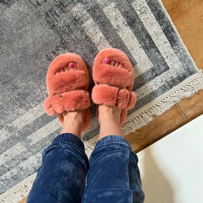 Person trägt rosa Plüschhausschuhe auf grauem Teppich, gemütliche Damenmode, Innenbereich.