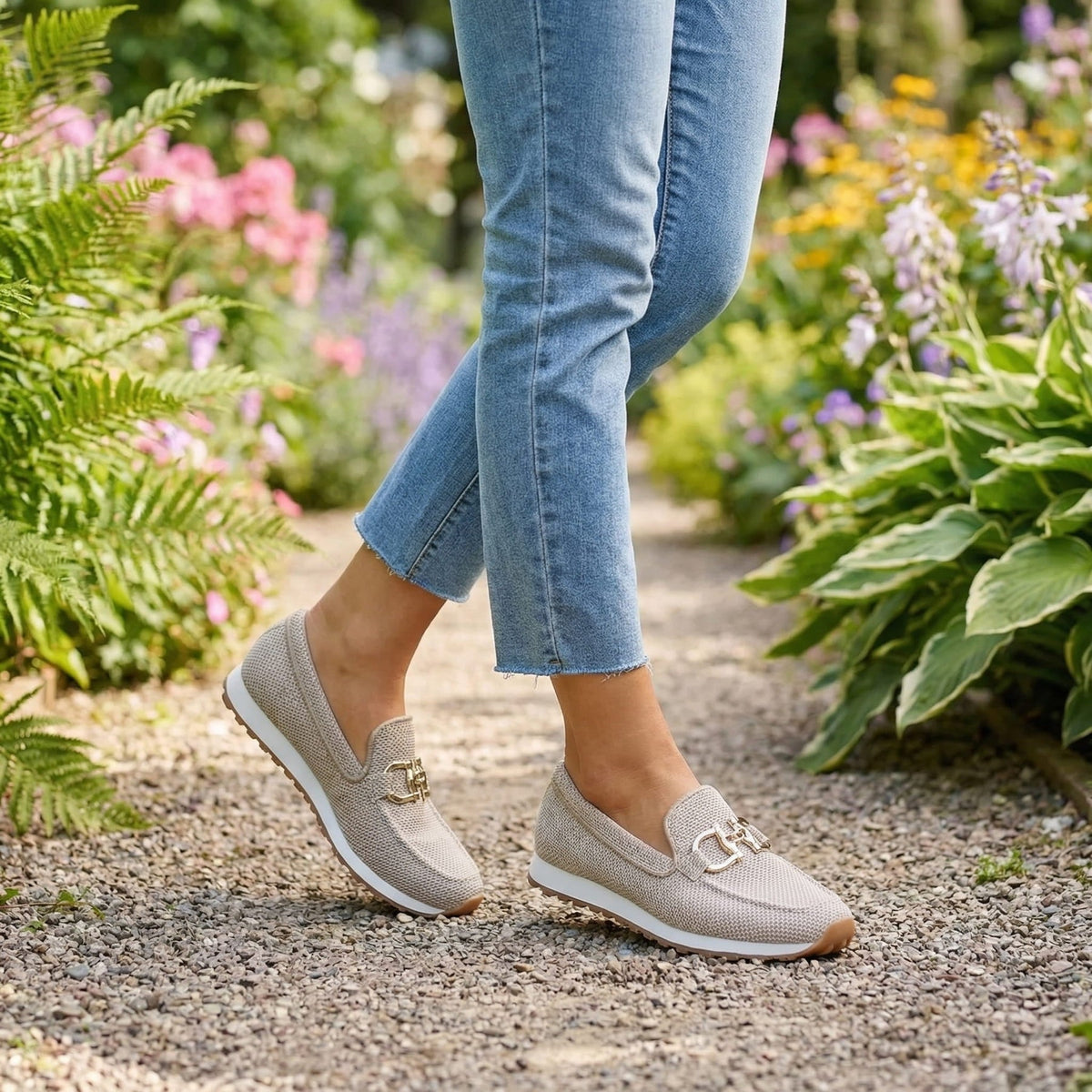Beige instegsskor på en kvinna som promenerar på grusgång i en blommande trädgård 11