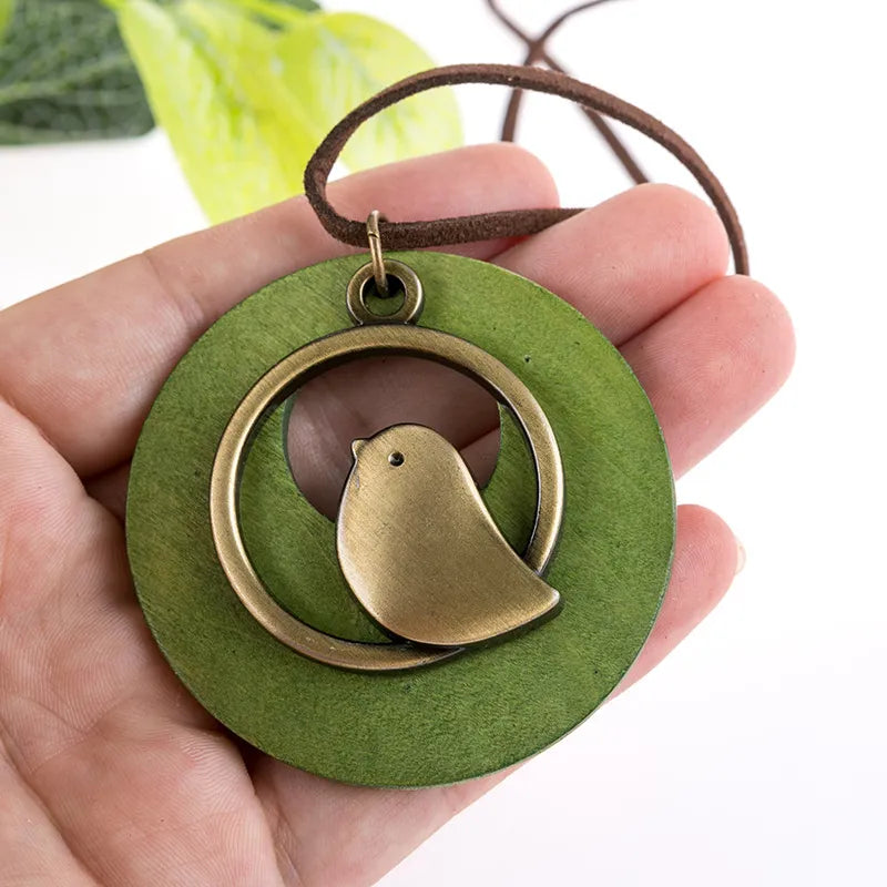 Grüner Holzanhänger mit bronzenem Vogelmotiv, handgefertigter Schmuck, Naturdesign.