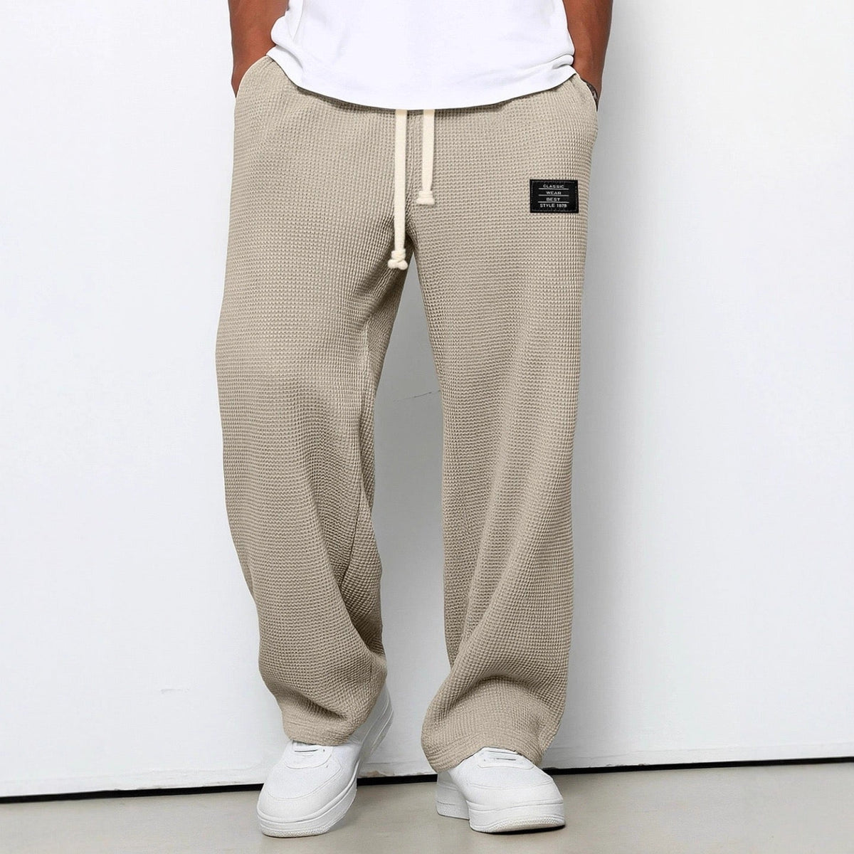 Man bär beige våffelstickade byxor med vida ben och krämvit dragsko, i närmare beskärning framifrån med vita sneakers. 6