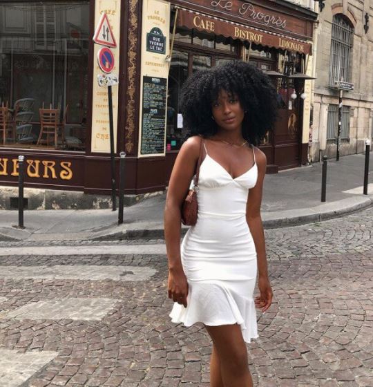 Frau in weißem Sommerkleid auf Kopfsteinpflasterstraße vor Café in Paris.