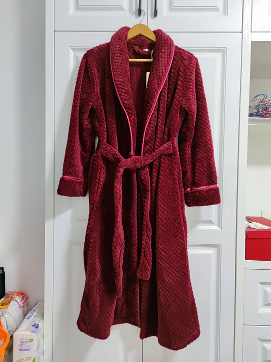 Roter Frottee-Bademantel mit Gürtel, hängend an weißem Schrank, gemütlich und luxuriös.