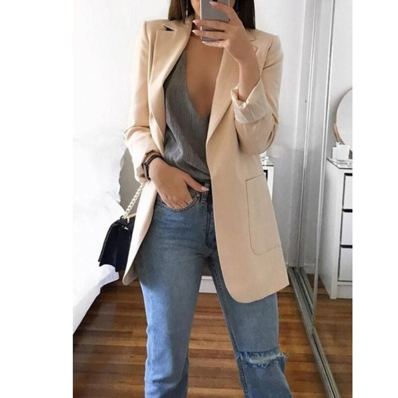 Frau in beigem Blazer, grauem Top und blauen Jeans, modisch, lässig, Spiegel-Selfie.