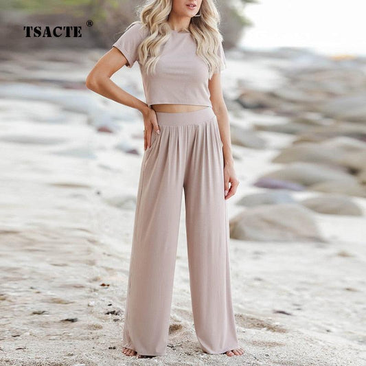 Frau in beigem zweiteiligem Set am Strand, lässige Sommermode, T-Shirt und weite Hose.