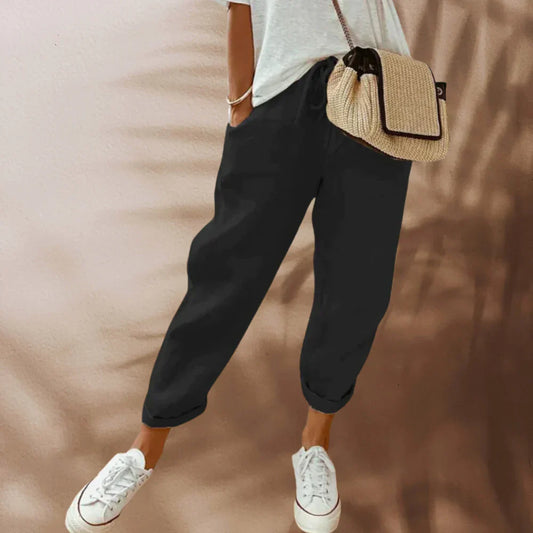 Frau in schwarzer Jogginghose, weißem T-Shirt, Strohtasche, weiße Sneaker, lässiger Stil