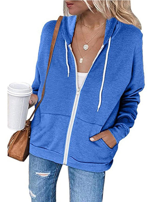 Frau in blauer Kapuzenjacke mit Reißverschluss, Kaffeebecher, Jeans, braune Tasche, lässiger Look.