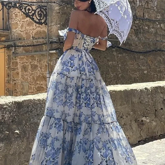 Frau in blau-weißem, schulterfreiem Blumenkleid mit Spitze, hält weißen Sonnenschirm.