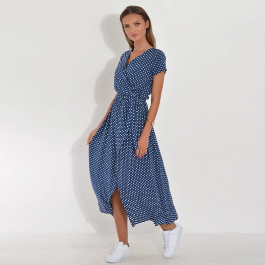 Frau im blauen gepunkteten Sommerkleid mit weißen Sneakers vor weißem Hintergrund.