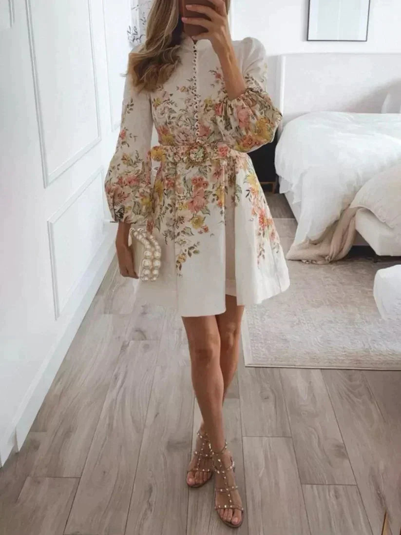 Frau in weißem Blumenkleid mit Perlenhandtasche und Sandalen im Schlafzimmer.