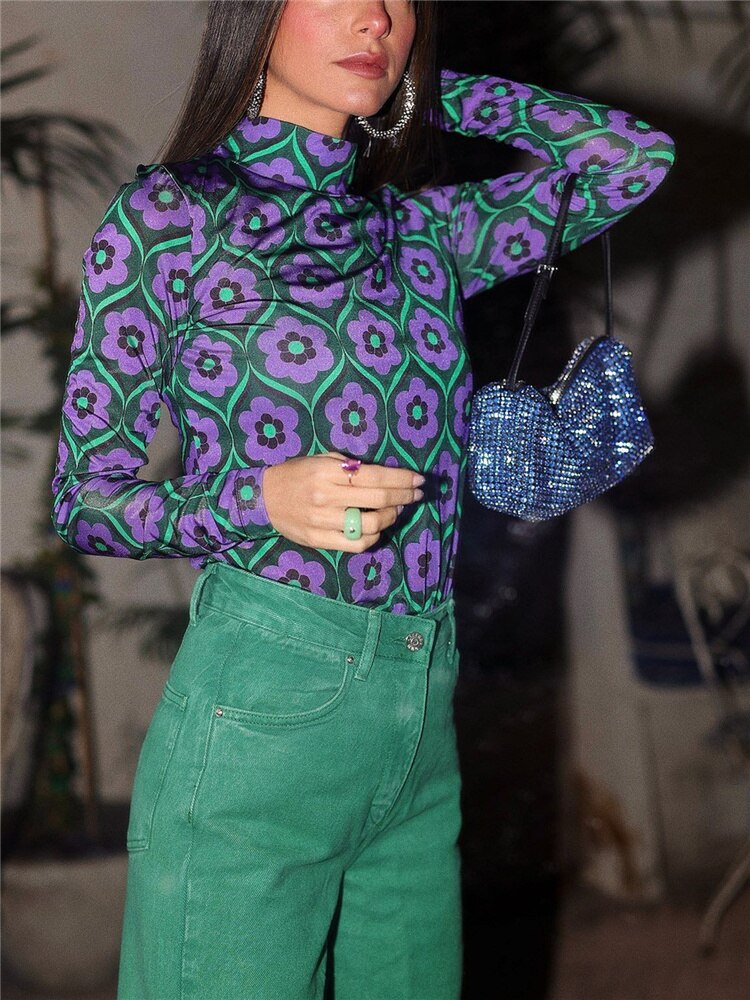 Frau in lila-grünem Blumen-Top, grüner Hose, mit blauer Glitzertasche, modisch, stilvoll.