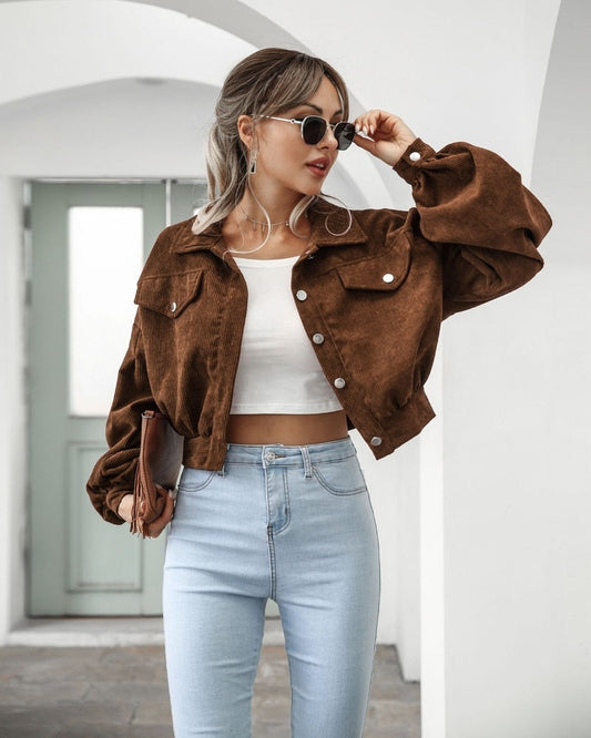 Frau in brauner Cordjacke, weißem Top, blauer Jeans, Sonnenbrille, modisch, urbaner Stil.