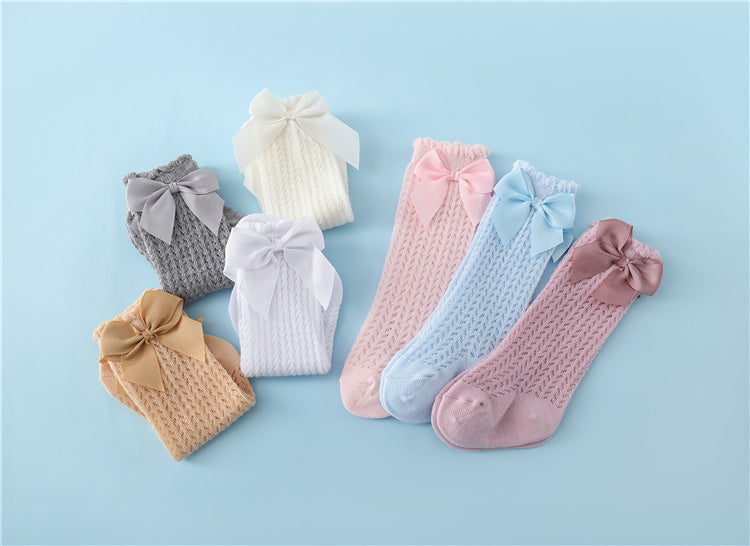 Sieben Paar bunte Babysocken mit Schleifen auf blauem Hintergrund.