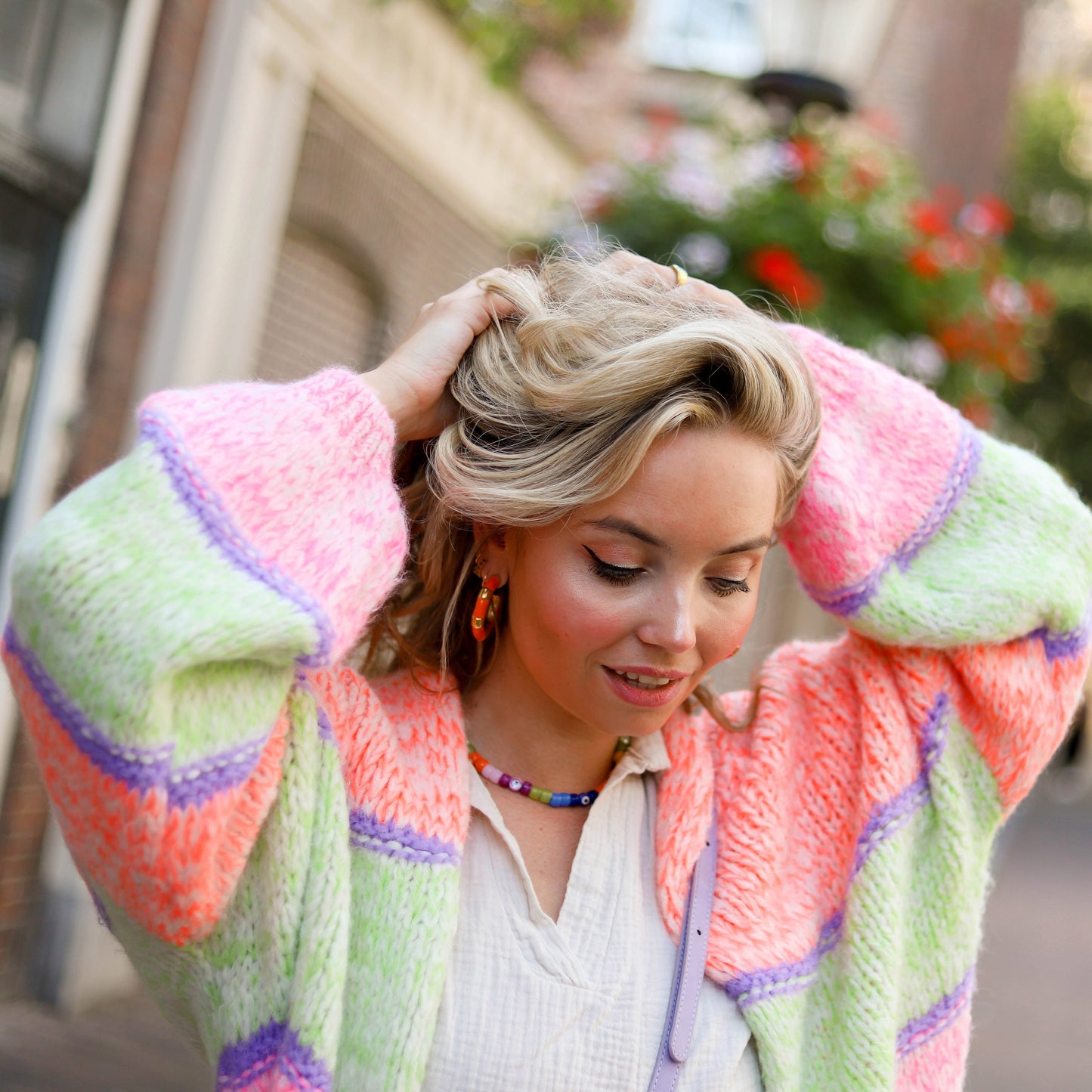 Frau in bunter Strickjacke, pastellfarben, lässiger Stil, modisch, draußen, Blumen im Hintergrund.