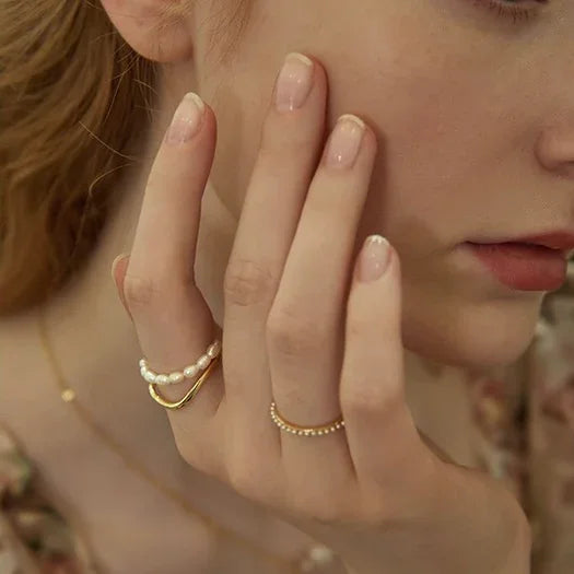 Frau mit goldenen und perlenbesetzten Ringen, Nahaufnahme, elegante Schmuckmode, zarte Hände.