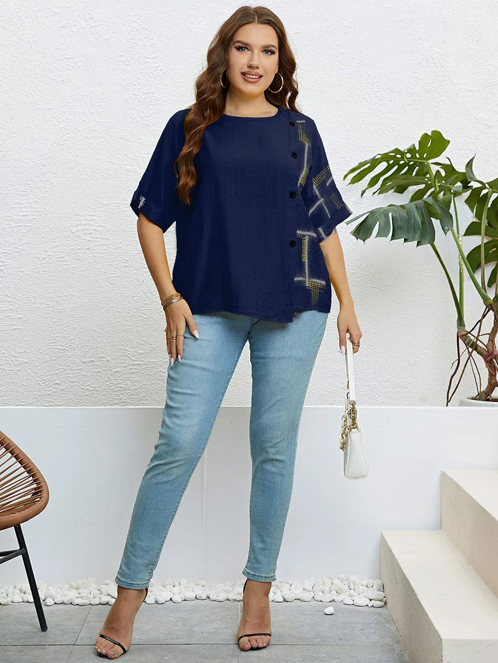 Frau in dunkelblauer Bluse und blauer Jeans, steht vor weißer Wand, modisch, lässig.