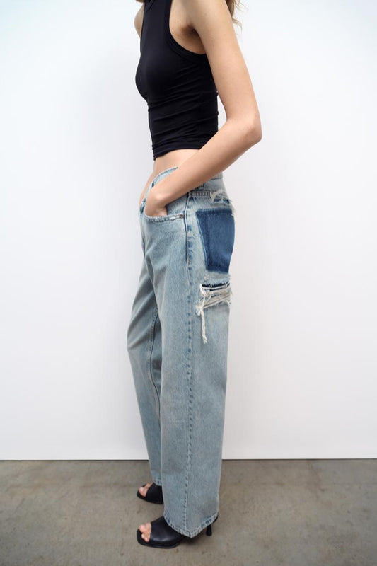 Frau in zerrissener Jeans und schwarzem Top, seitlich, auf Betonboden.