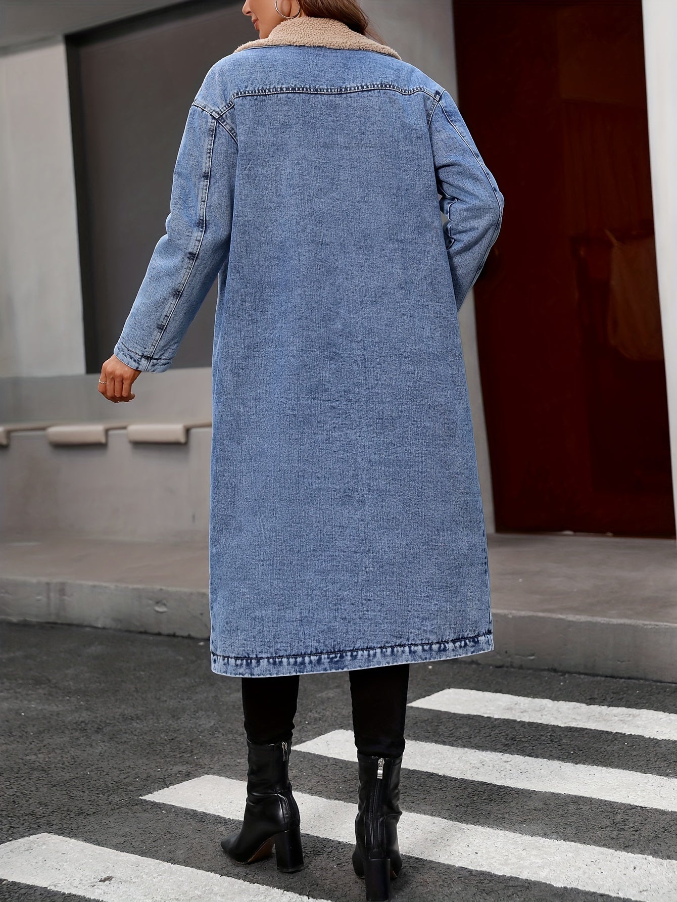 Frau in langem, blauem Jeansmantel auf Straße, schwarze Stiefel, modisch, urbaner Stil.