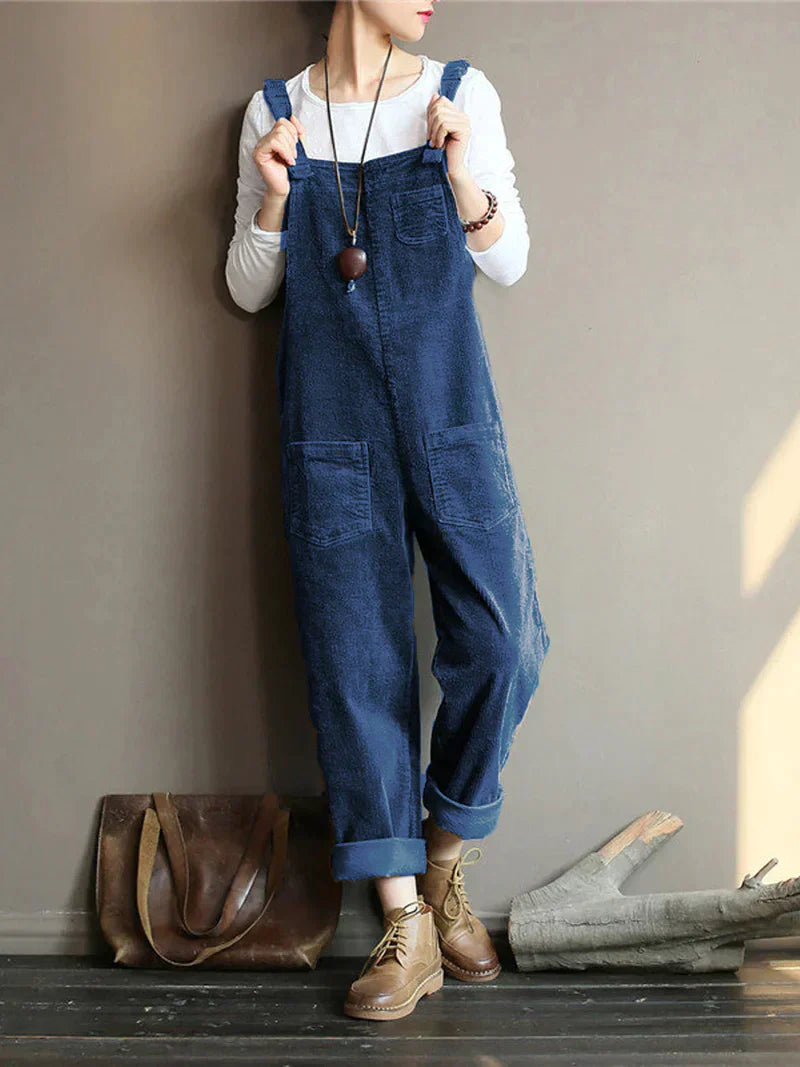 Frau in blauer Latzhose aus Denim, weißem Langarmshirt, braunen Stiefeln, brauner Ledertasche.