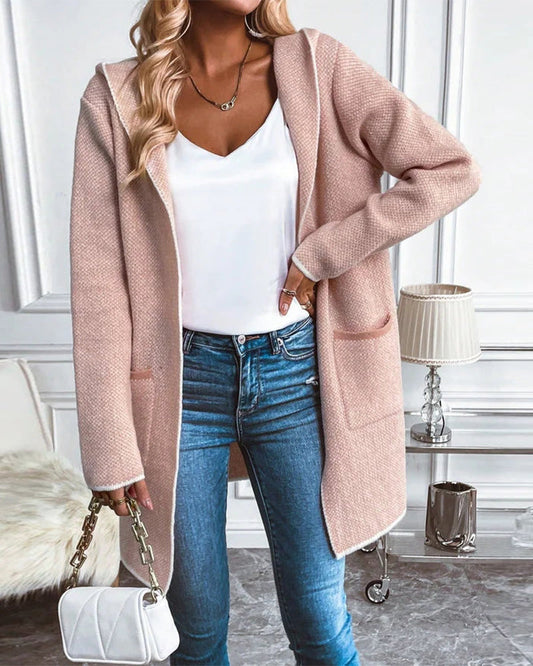 Frau in rosa Strickjacke, weißem Top, blauer Jeans, hält weiße Handtasche, modisch, elegant.