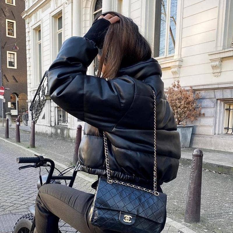 Frau in schwarzer Lederjacke auf Fahrrad, Chanel-Tasche, städtische Straße, Wintermode.