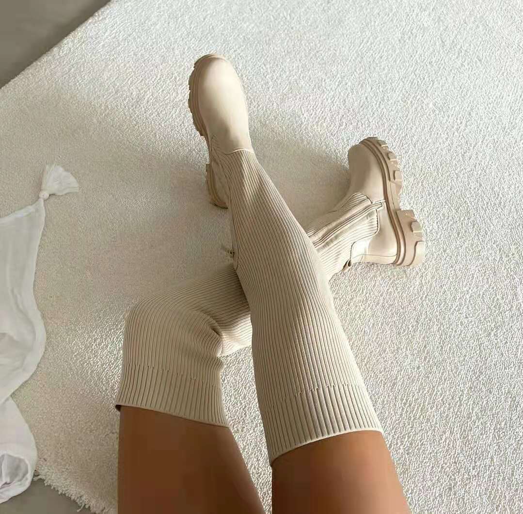 Beige kniehohe Stiefel mit gerippter Struktur auf weißem Teppich, modisch und elegant.