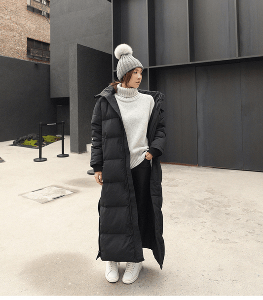 Frau im schwarzen, übergroßen Parka, Wintermantel, grauer Pullover, weiße Mütze, urbaner Hintergrund.
