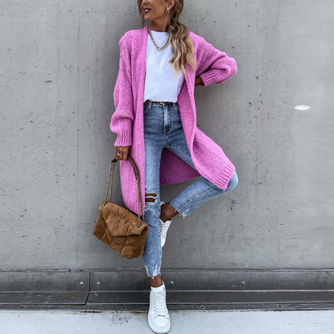 Frau in rosa Strickjacke, weiße Bluse, zerrissene Jeans, braune Tasche, weiße Sneaker.