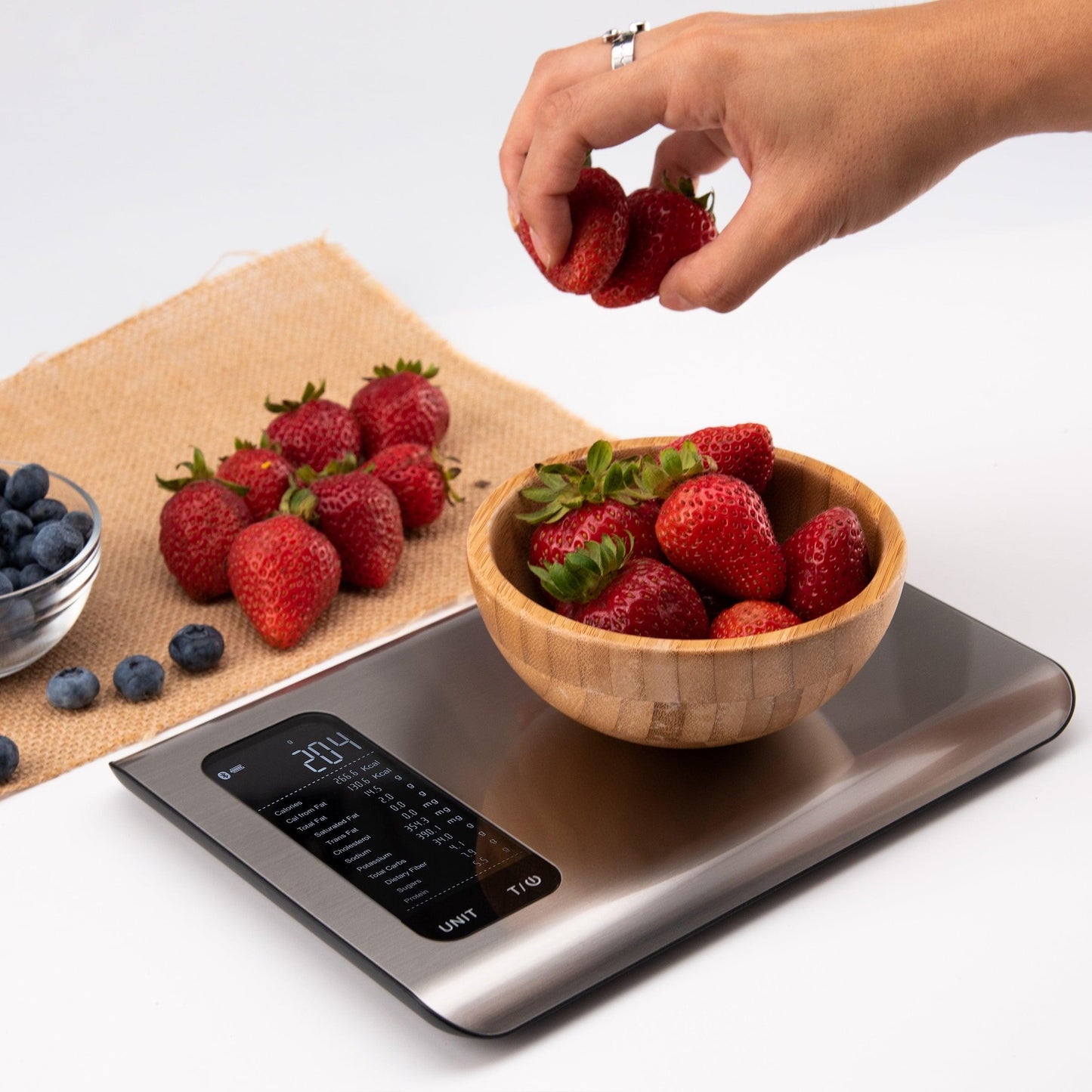 Digitale Küchenwaage aus Edelstahl mit Erdbeeren in Holzschale, moderne Lebensmittelwaage.